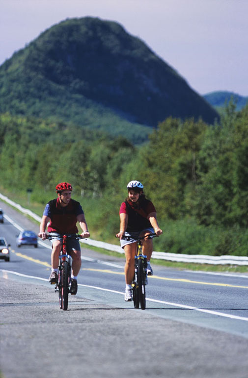 Colour photograph of two cyclists, highway and mountain in background