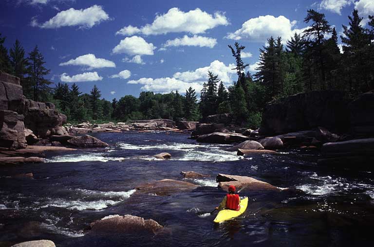 Colour photograph of person in yellow kayak, shooting rapids