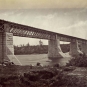 Photographie noir et blanc d'un pont ferroviaire avec piliers de granite enjambant une rivière