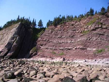 Photographie couleur dun rivage rocailleux et de hautes formations de roc rouge surmontées darbres