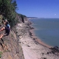 Colour photograph rock cliff along a shoreline and two people rock climbing