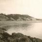 Black and white photograph of a shoreline with high cliffs and a house on top